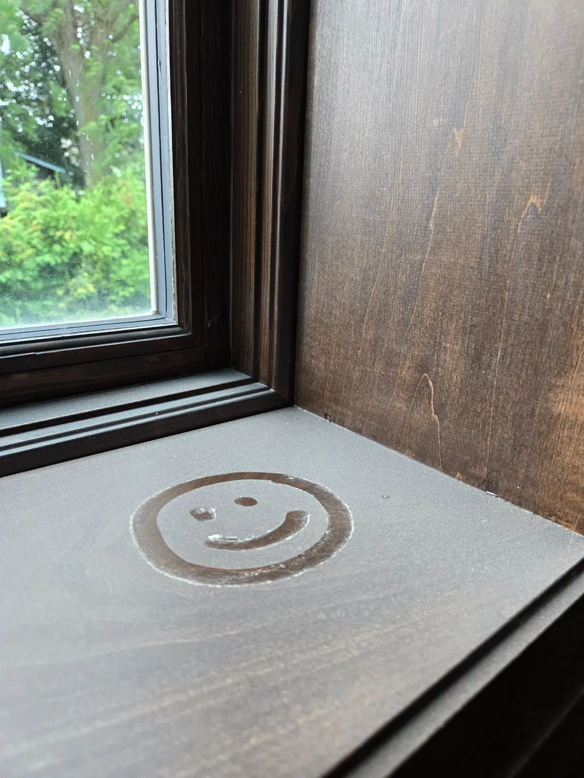 Window sill covered in fine construction dust with a smiley face drawn in the dust surface